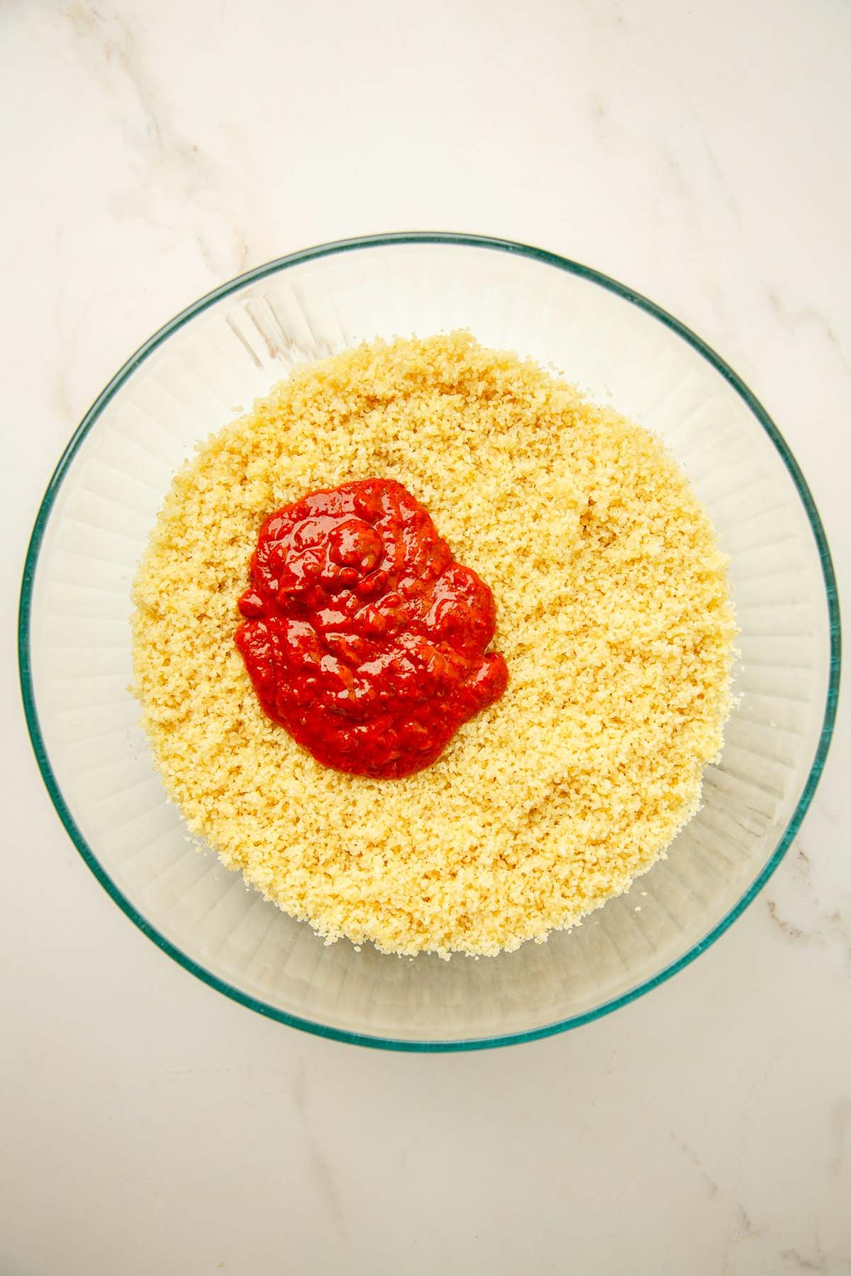 Fine bulgur topped with Turkish red pepper paste (salça) in a glass bowl, ready to be mixed.