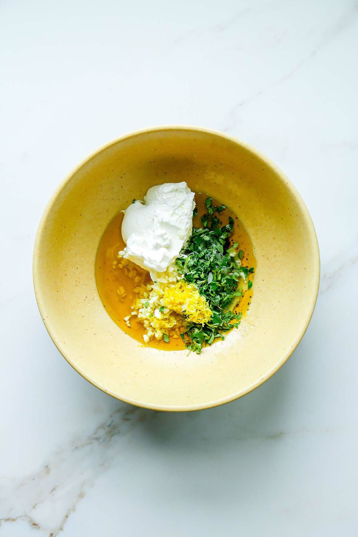 Greek yogurt, olive oil, lemon juice, garlic, and herbs arranged in a bowl before mixing