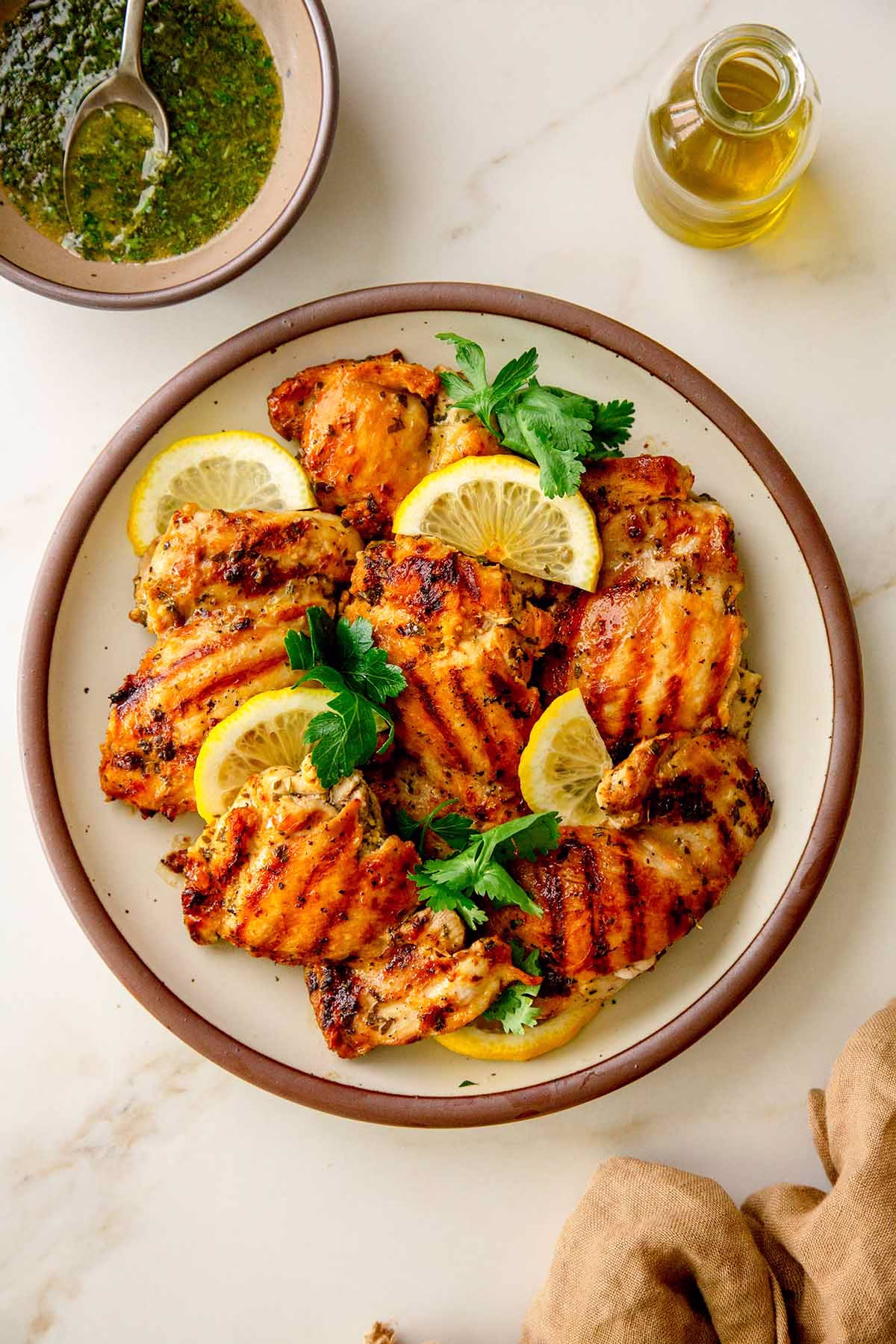 Grilled chicken thighs with golden grill marks, topped with lemon herb sauce and fresh herbs