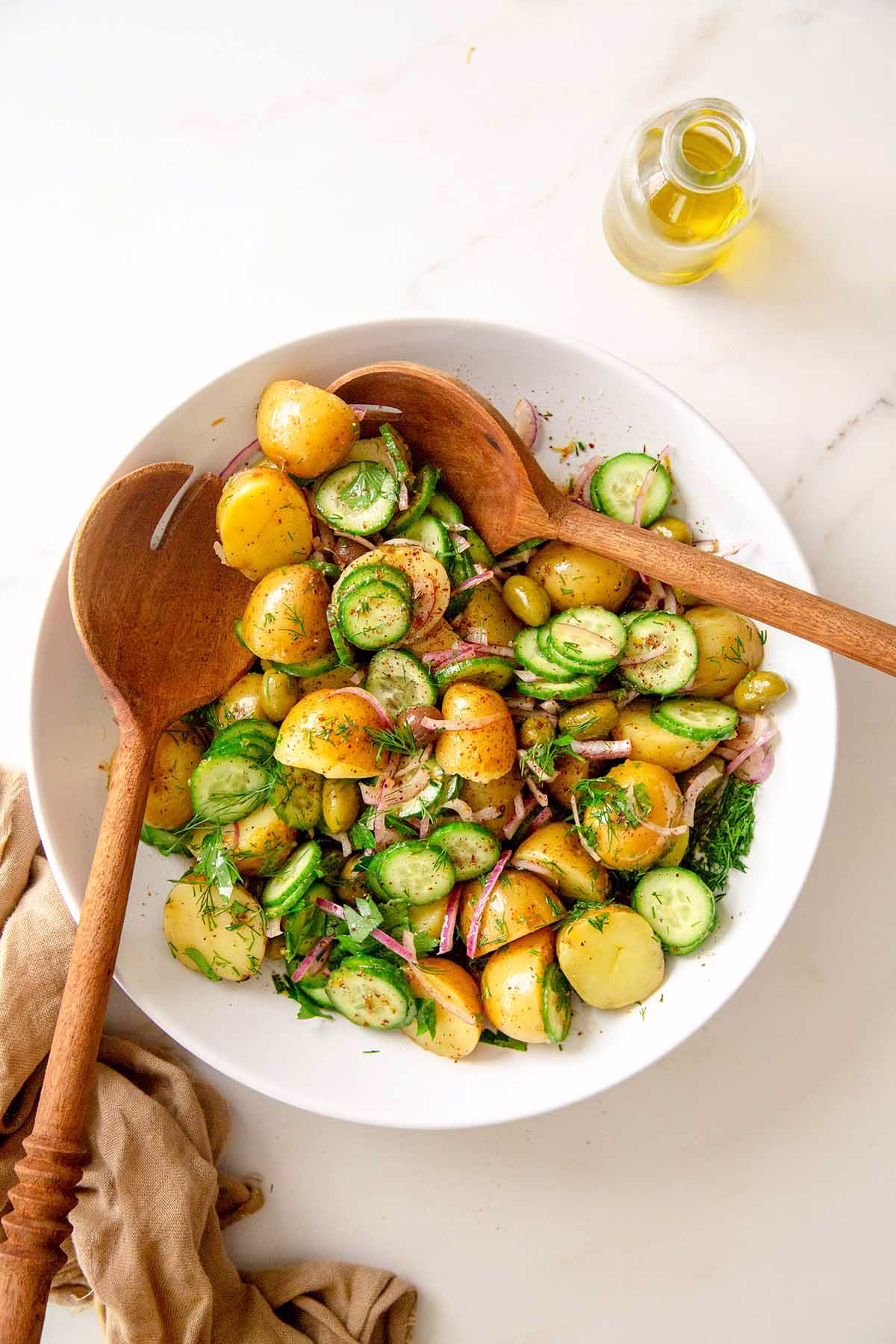 Overhead shot of Mediterranean potato salad with baby potatoes, cucumber, red onion, olives, fresh herbs, and sumac dressing. 