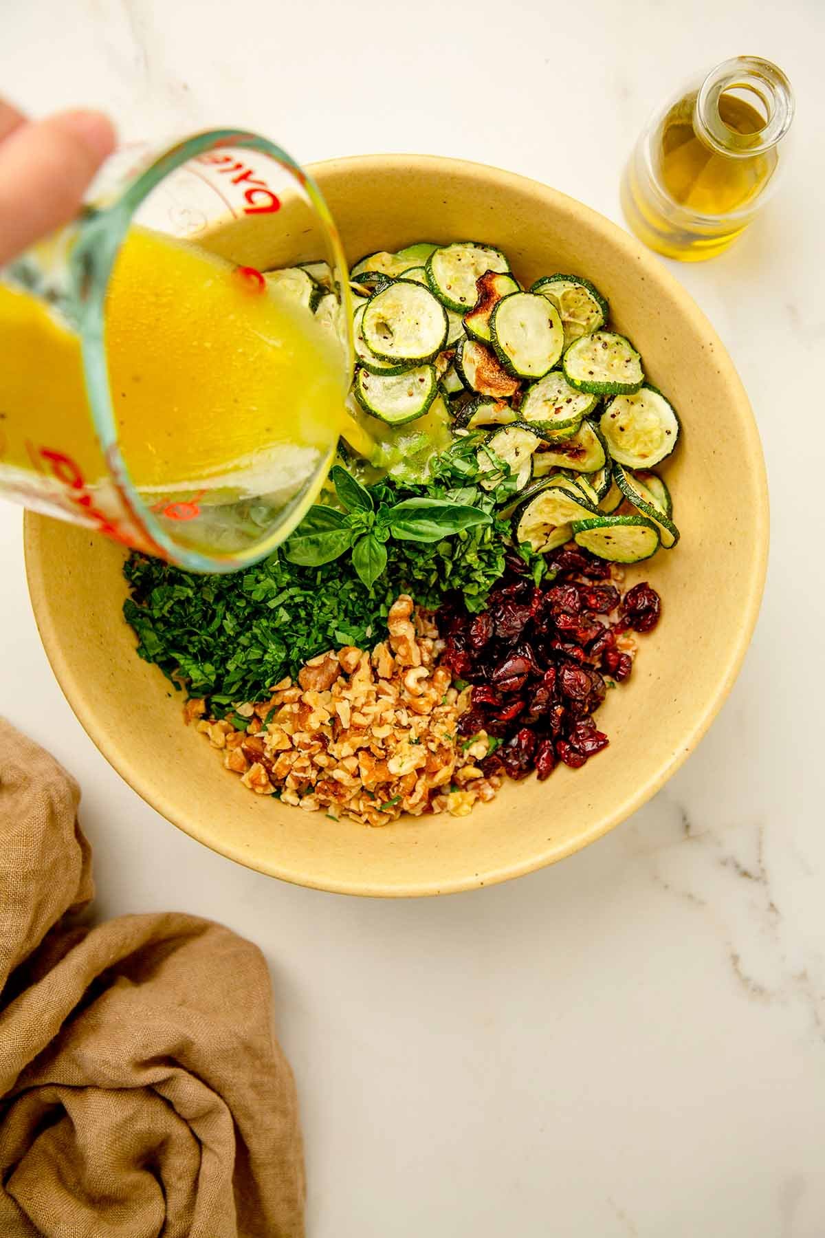 Lemon vinaigrette being poured over a farro and zucchini salad