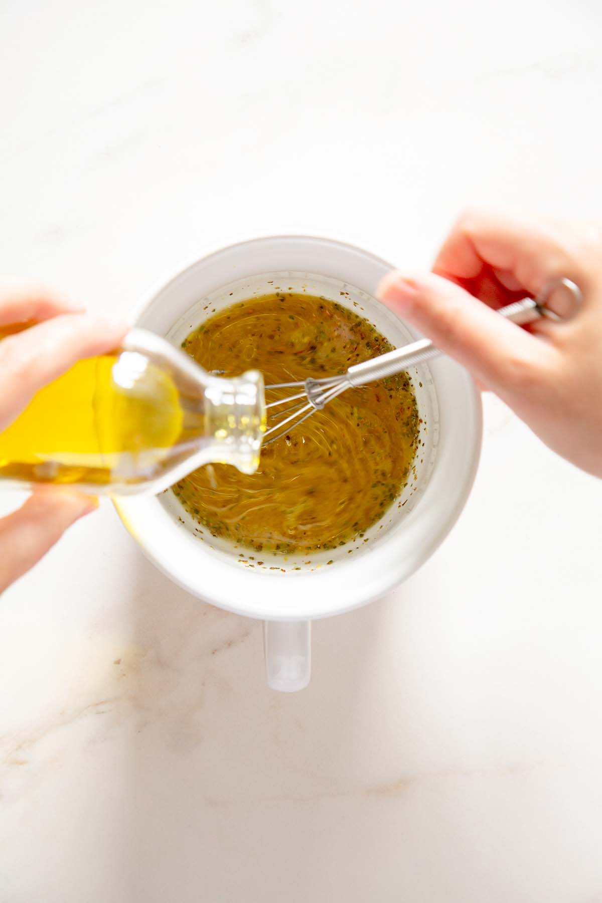 pouring olive oil into lemon juice, herbs and garlic