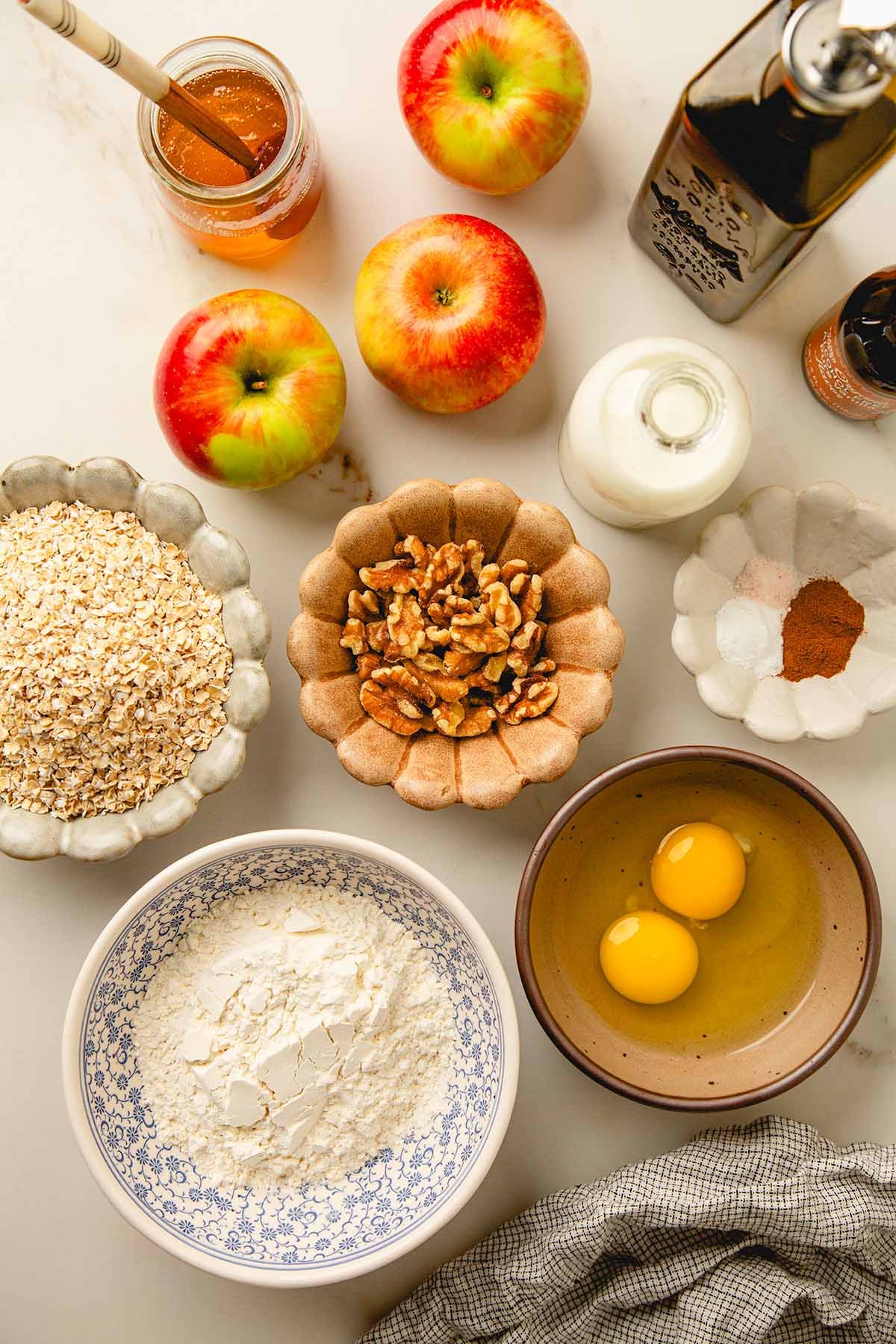 A flat lay of all the ingredients together, including oat, flour, honey, apples, milk, oil, spices, and vanilla