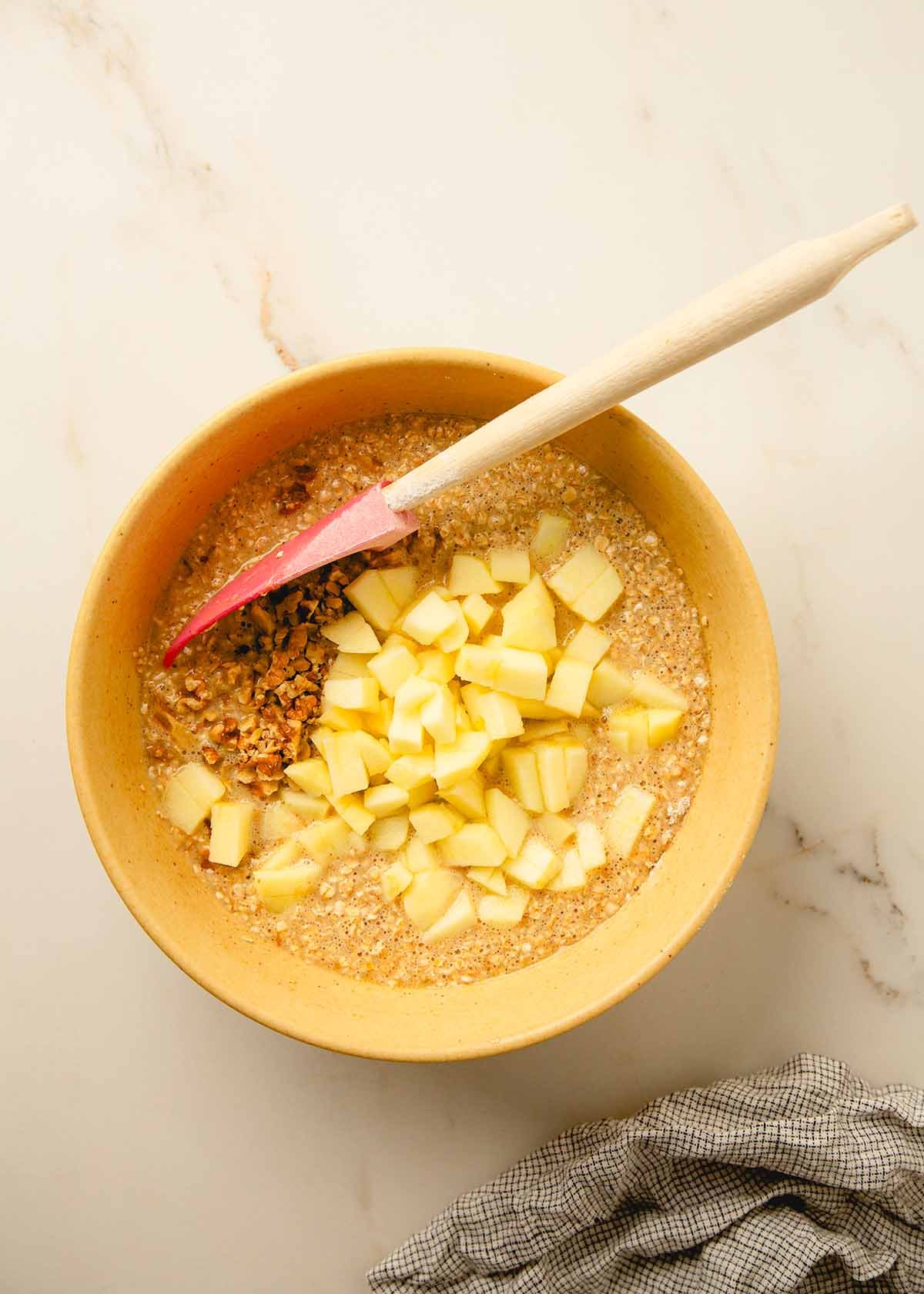 Diced apples and walnuts being folded into muffin batter.