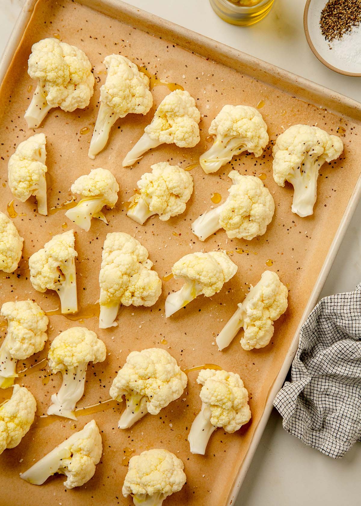 Cauliflower florets placed on a parchment-lined baking sheet with olive oil, salt, and pepper before tossed together