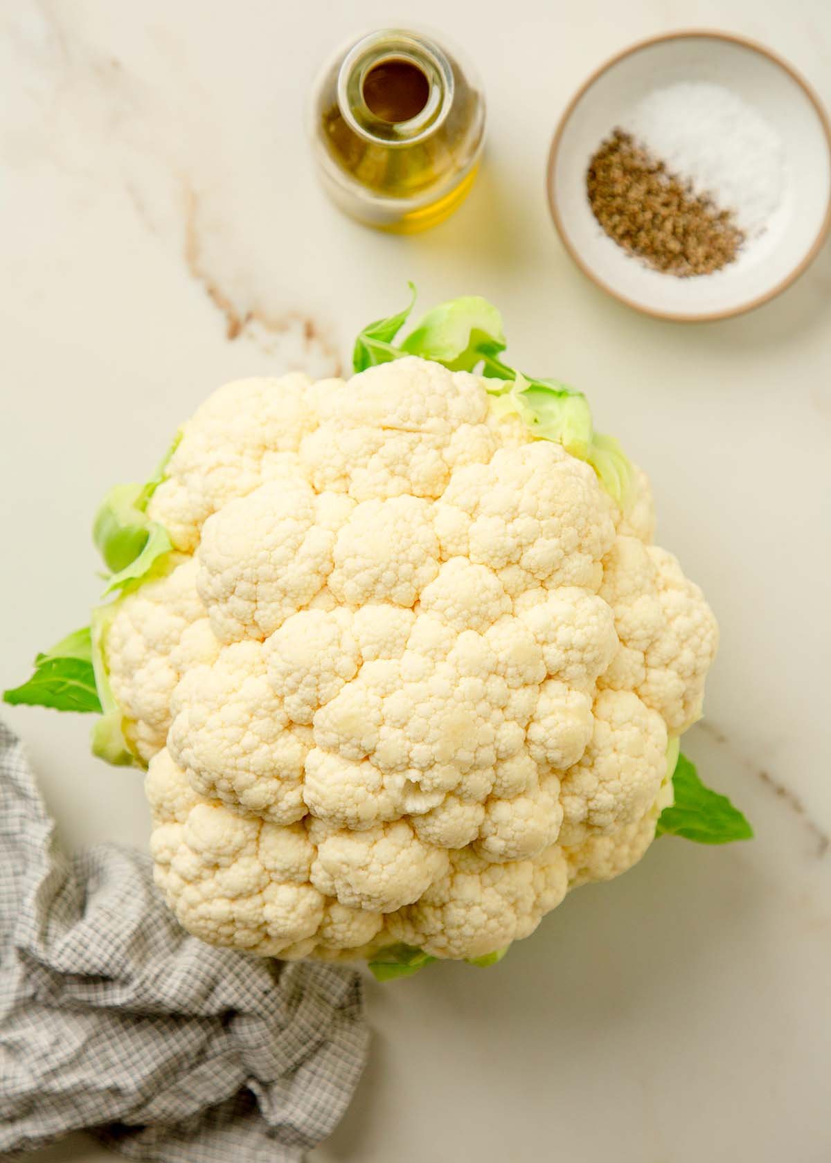 Cauliflower, olive oil, salt, and pepper on a white marble surface