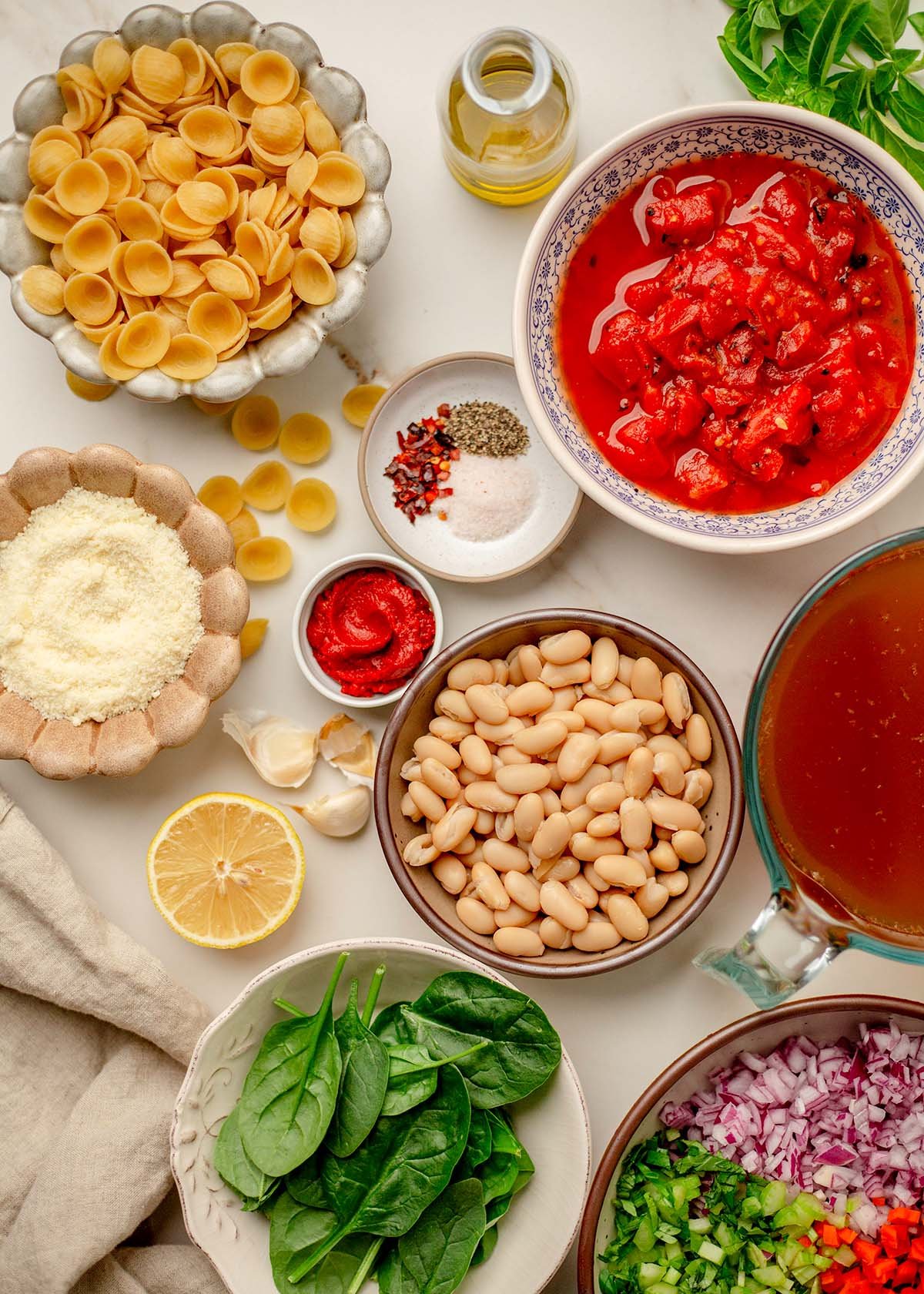 Ingredients for orecchiette soup laid out on a countertop pasta, spinach, white beans, garlic, and tomatoes.