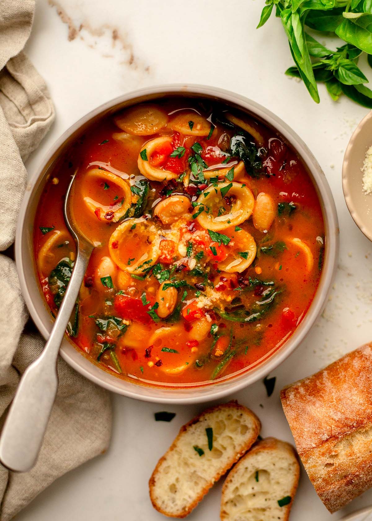 Bowl of orecchiette soup with spinach and white beans in a tomato broth.