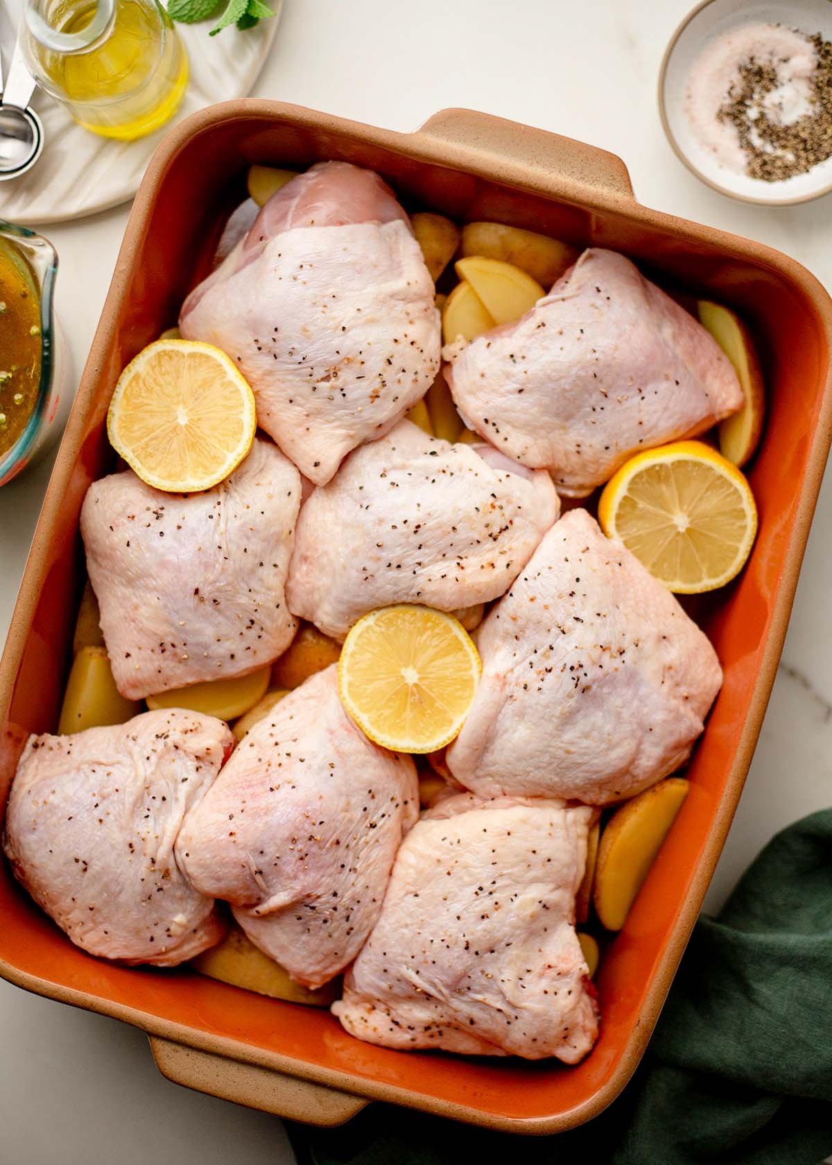 Raw chicken thighs over potatoes with sliced lemon