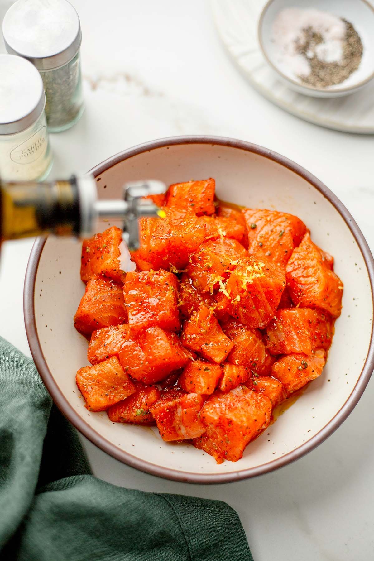 Salmon bites marinating in lemon and herbs before roasting for meal prep bowls.