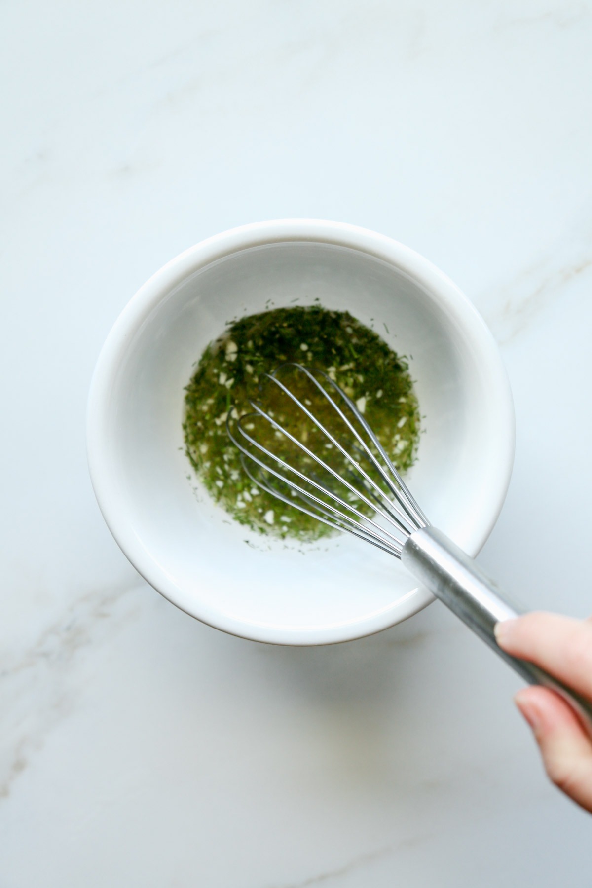 Dill, garlic, lemon juice, vinegar in a white bowl after being mixed