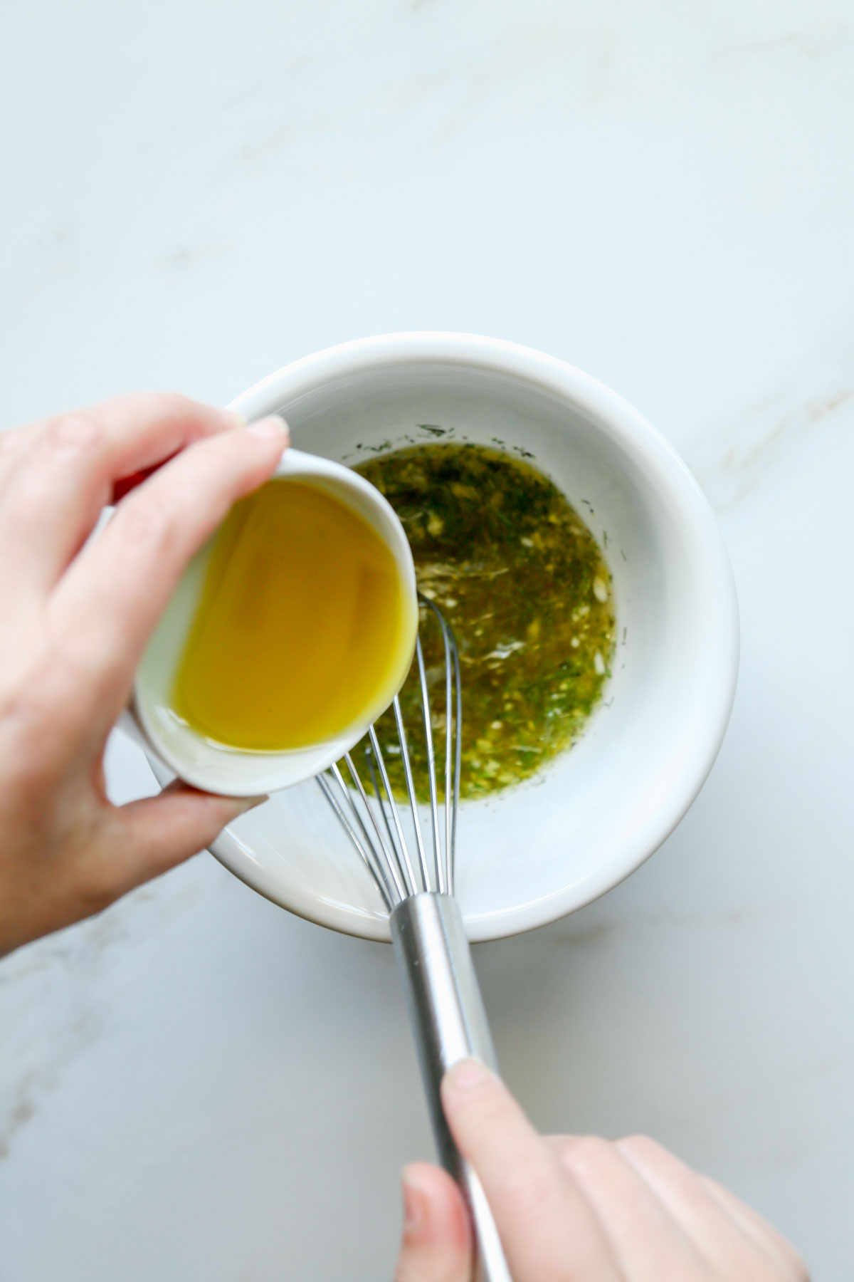Small bowl of olive oil added to vinegar and dill with spices