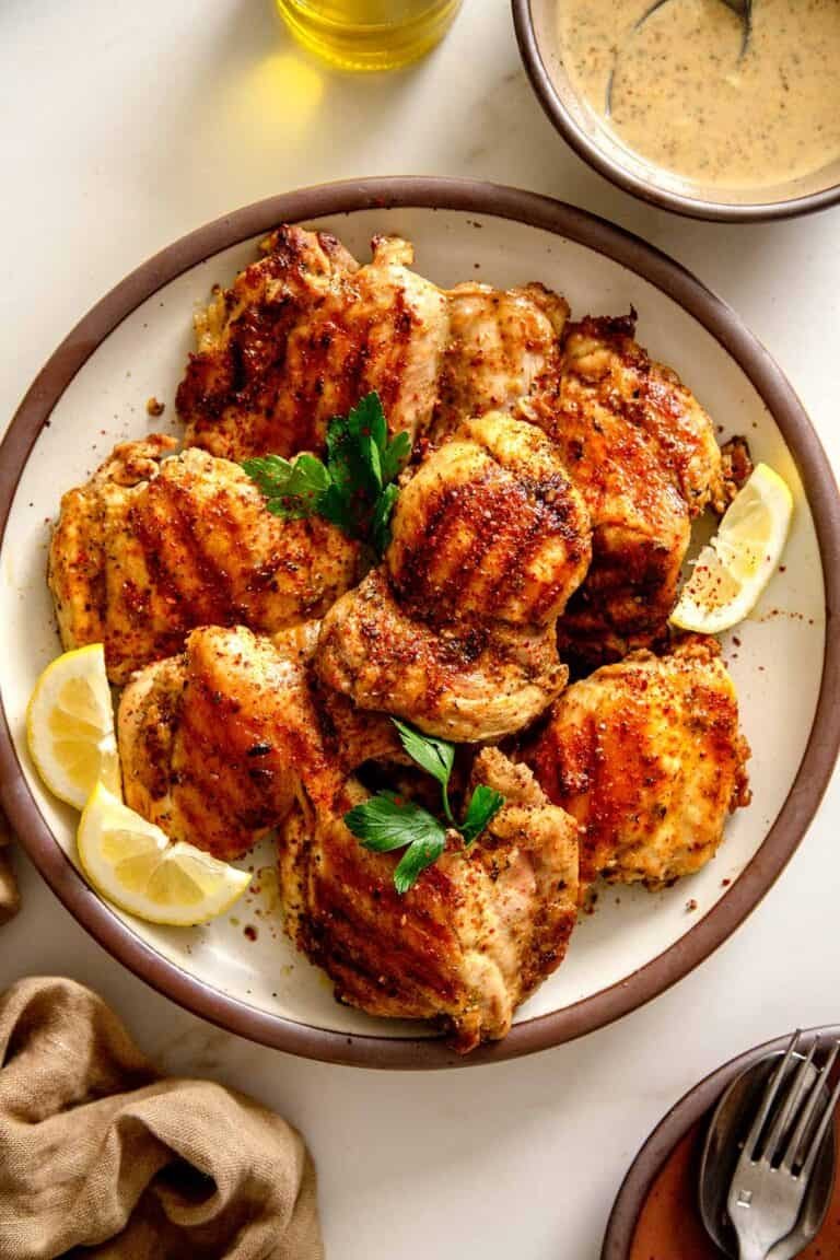 Plate of juicy grilled za'atar chicken thighs garnished with lemon wedges and parsley.