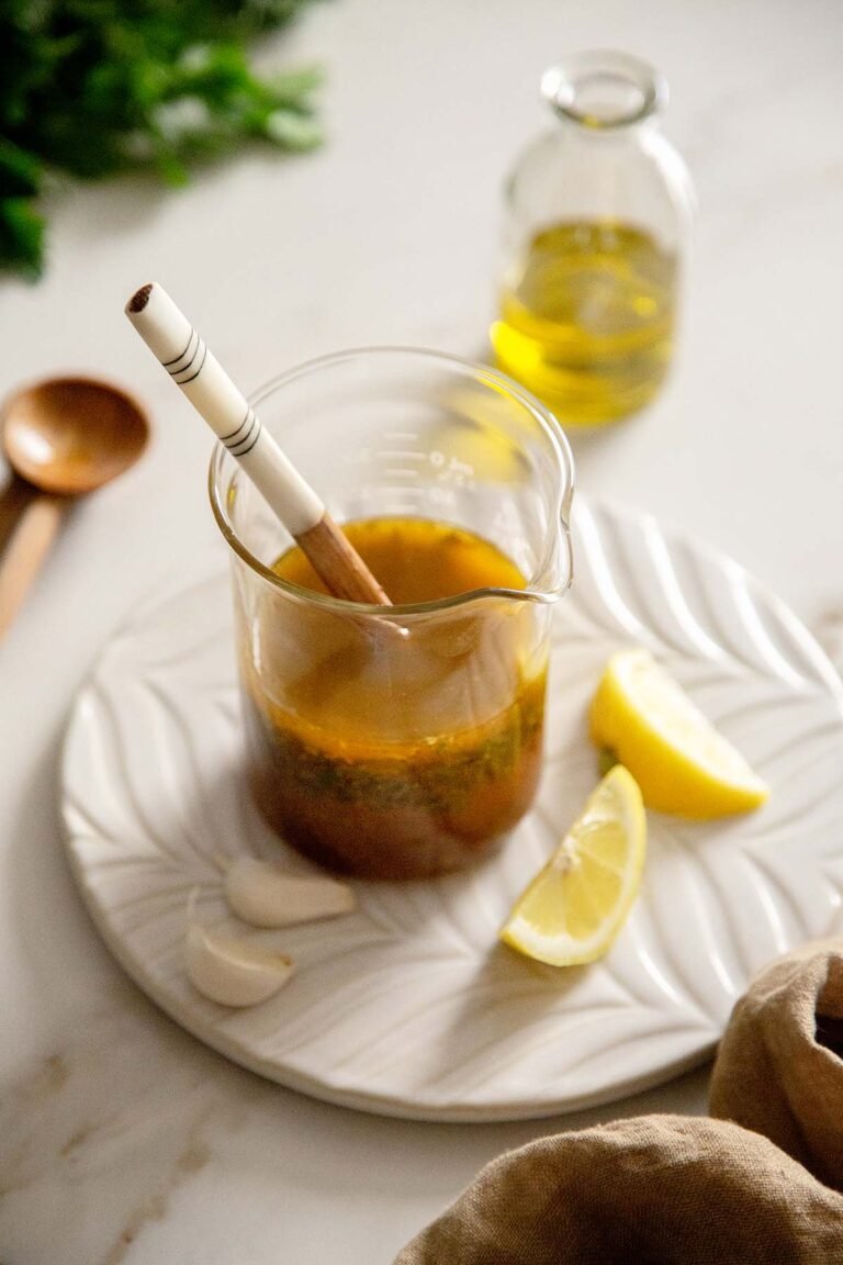 Mediterranean Lemon Garlic Vinaigrette in a beaker with lemon and garlic.