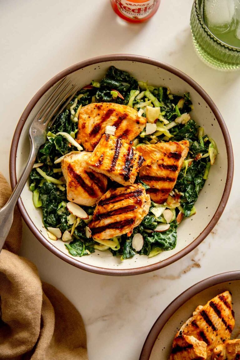 Overhead shot of Creamy Buffalo Kale Crunch Salad with Grilled Chicken Nuggets, featuring vibrant green kale and cabbage, golden-brown grilled chicken, and a creamy dressing drizzle.