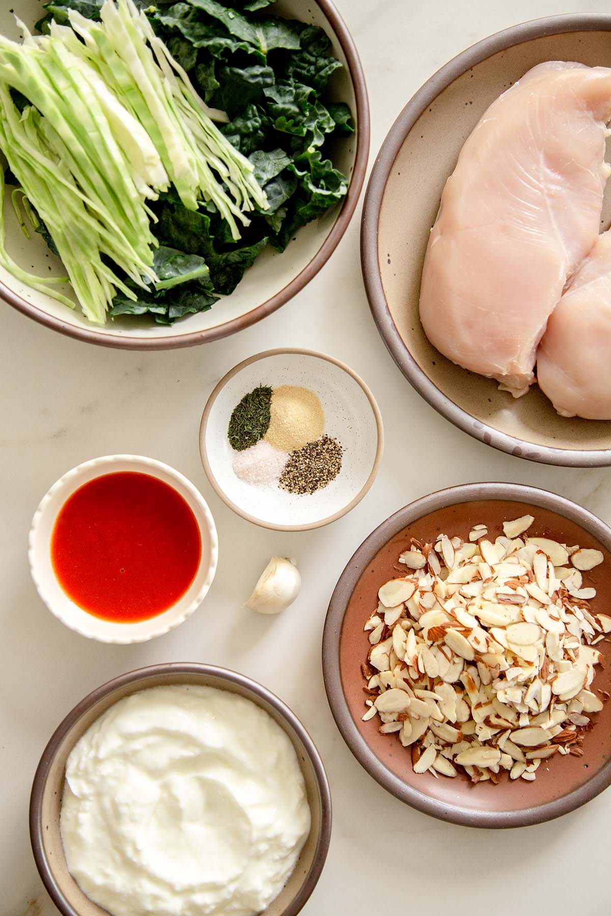 Ingredients for Creamy Buffalo Kale Crunch Salad with Grilled Chicken Nuggets: kale, cabbage, chicken, sour cream, hot sauce, almonds, and spices.