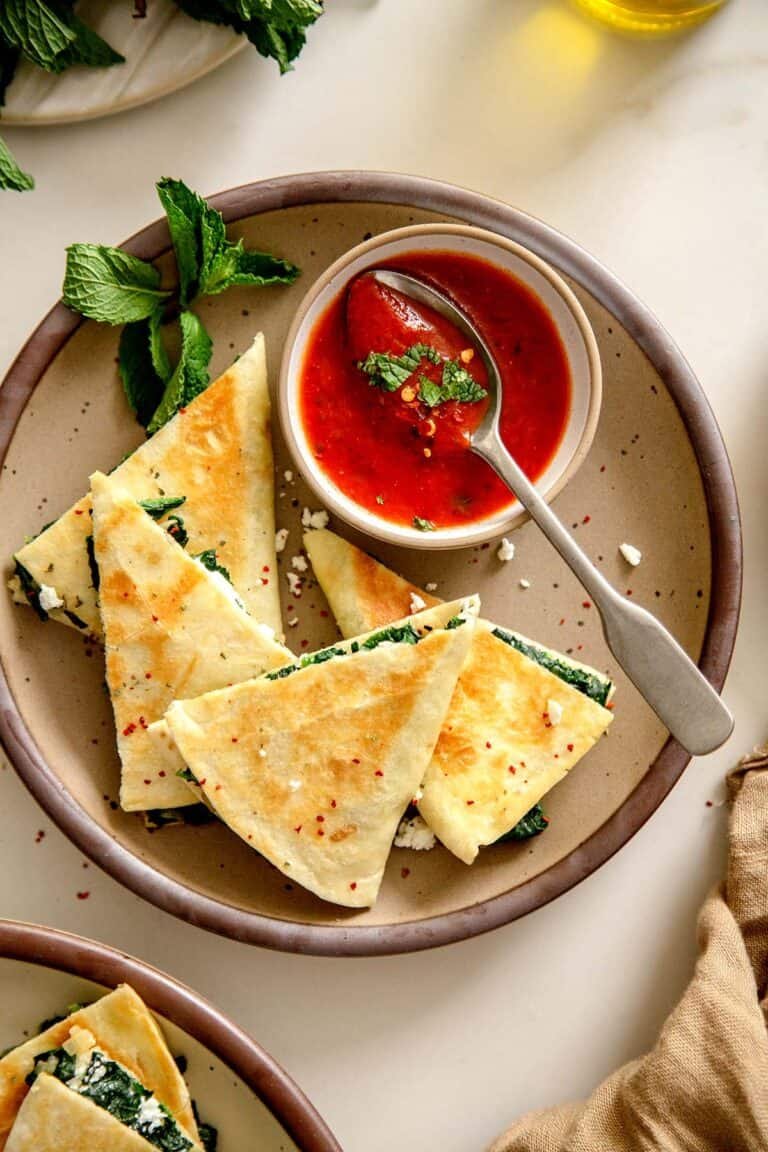 Close-up of golden brown Spanakopita Quesadilla wedges served with tomato sauce and fresh mint.