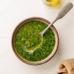 Bowl of lemony herb olive oil sauce with spoon on a marble surface