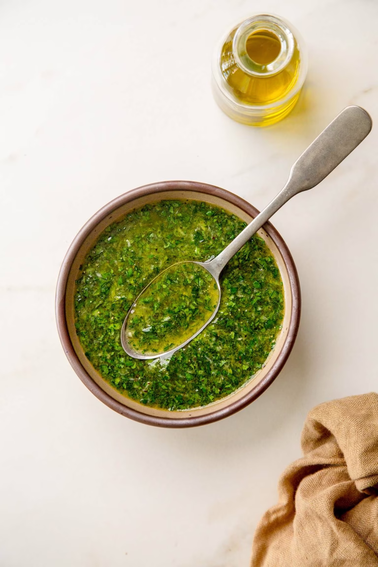 Bowl of lemony herb olive oil sauce with spoon on a marble surface
