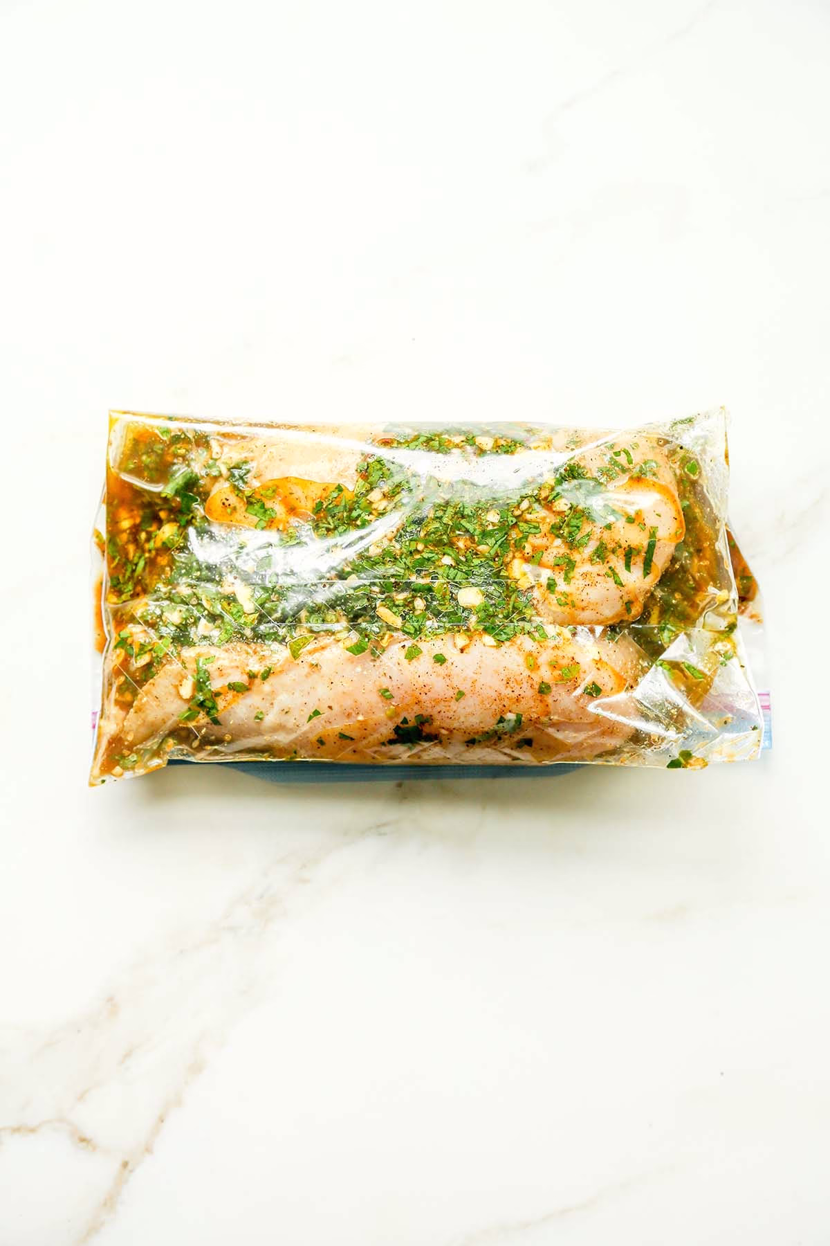 Raw chicken coated in herb marinade inside a resealable plastic bag