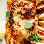 Greek yogurt marinated chicken thighs garnished with fresh oregano and lemon wedges