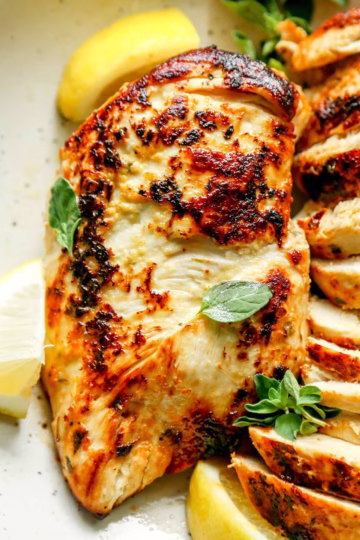 Greek yogurt marinated chicken thighs garnished with fresh oregano and lemon wedges