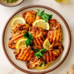 Grilled lemon herb chicken thighs on a white plate, garnished with fresh parsley and lemon wedges