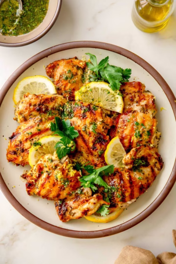 Grilled lemon herb chicken thighs on a white plate, garnished with fresh parsley and lemon wedges