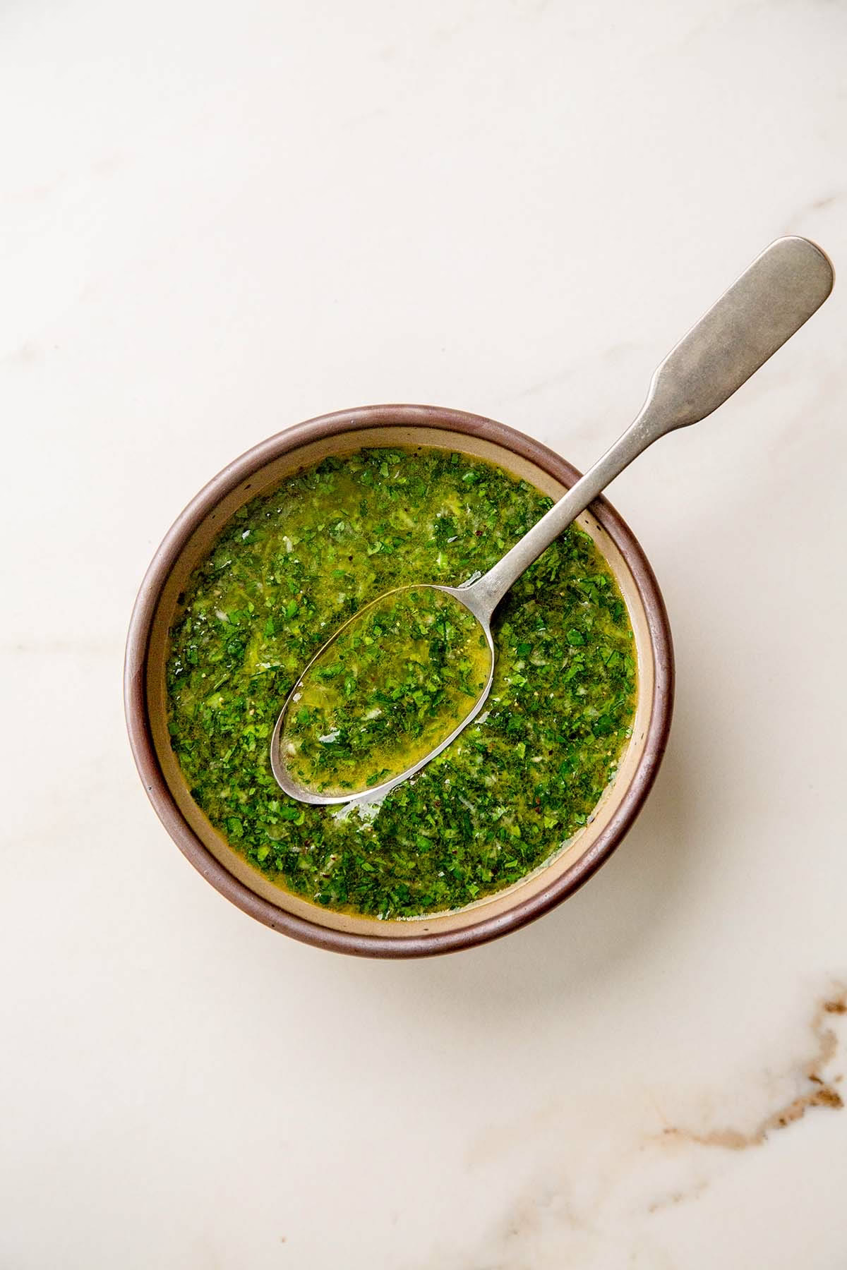 Bowl of lemony herb olive oil sauce with spoon on a marble surface