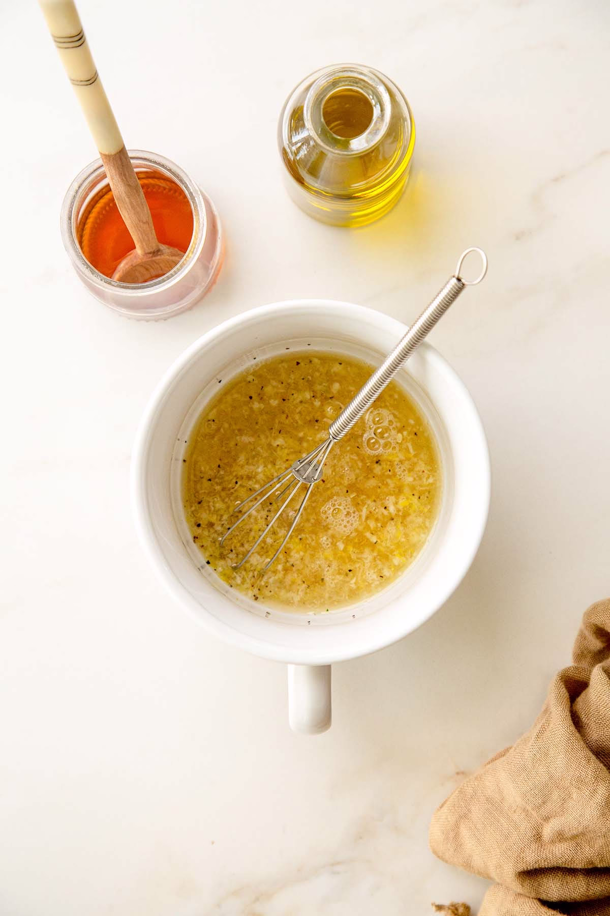 White bowl with whisk mixing lemon, garlic, olive oil, and seasonings for herb sauce base