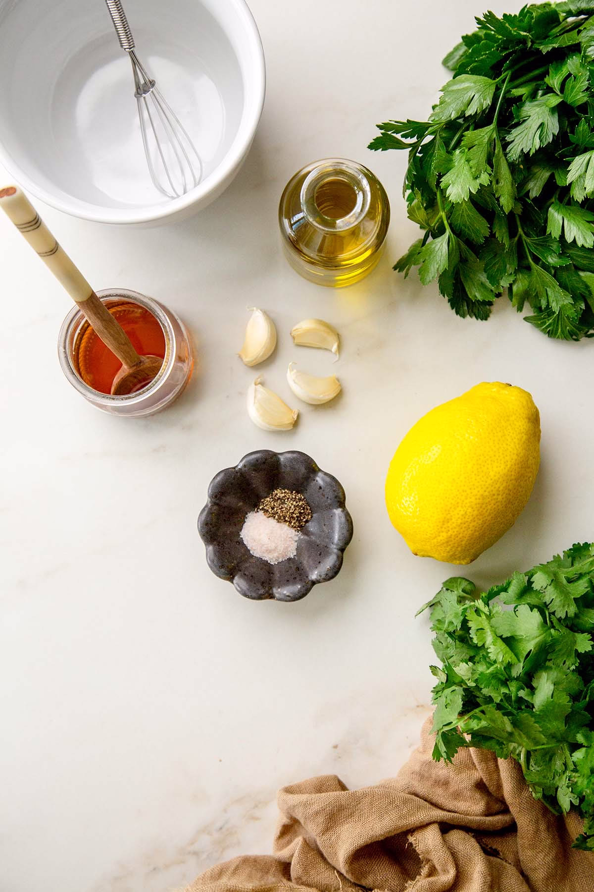 Flat lay of fresh ingredients for lemony herb olive oil sauce, including parsley, cilantro, garlic, lemon, olive oil, and maple syrup