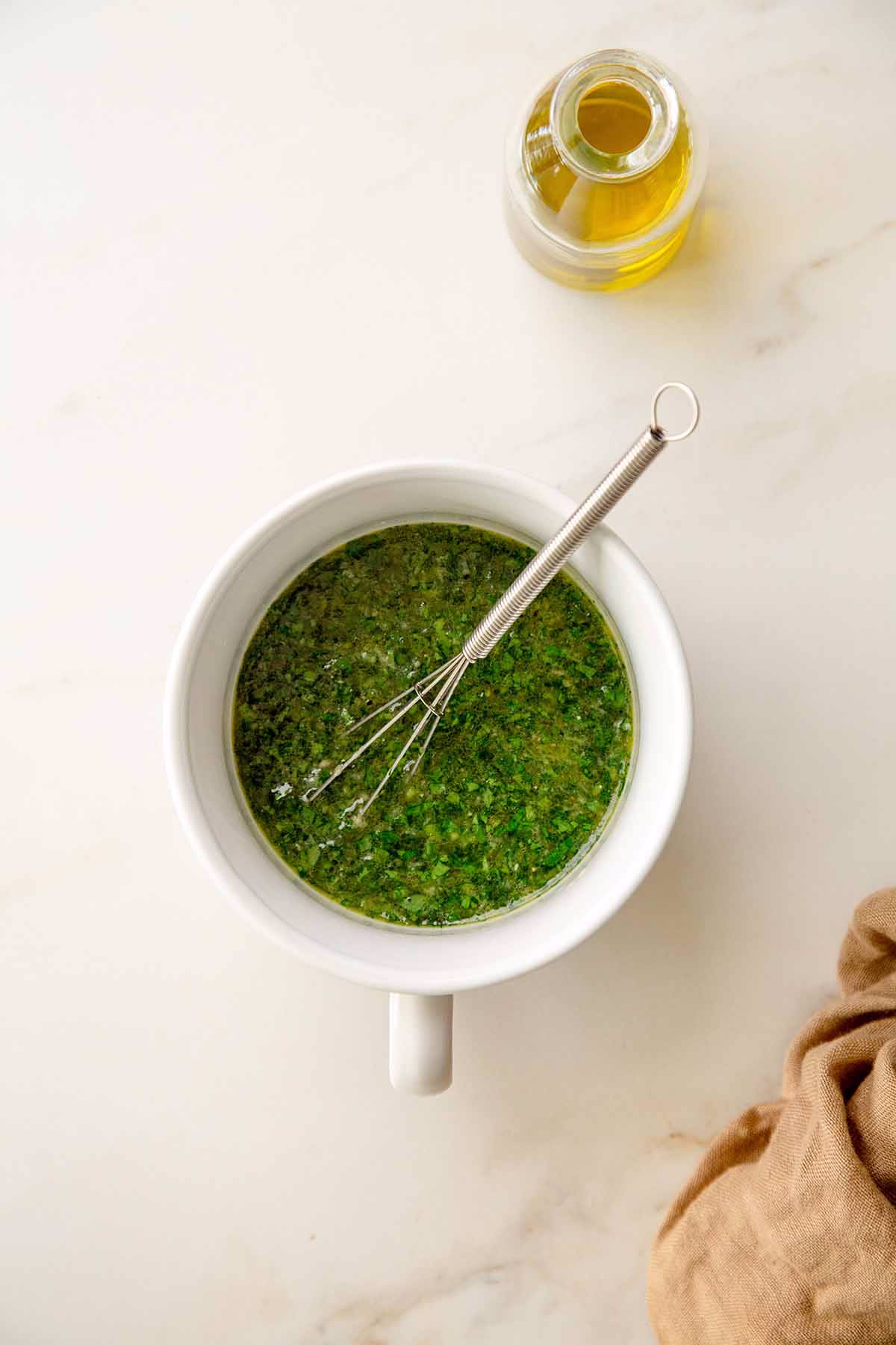 Chopped parsley and cilantro added to a lemon-garlic olive oil base in a white mixing bowl