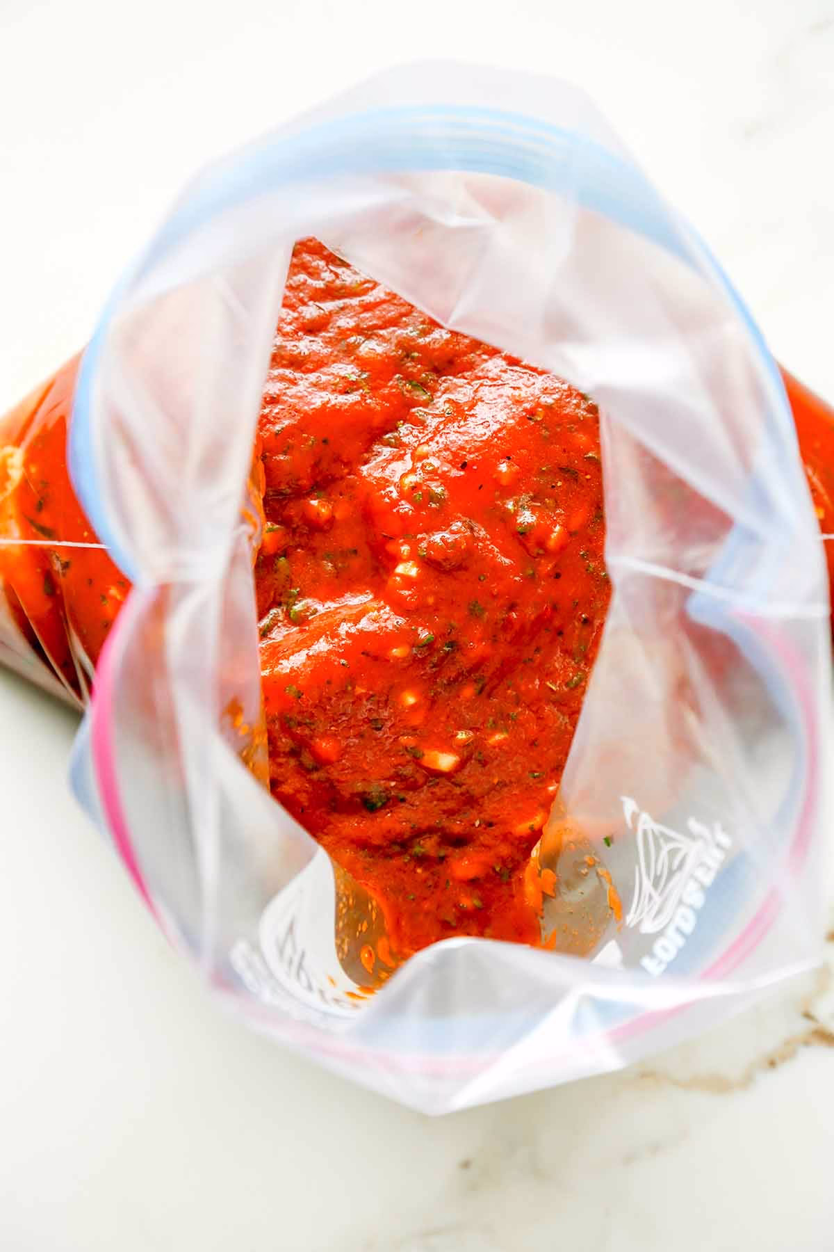 Raw chicken pieces coated in Turkish red pepper marinade inside a zip-top bag.