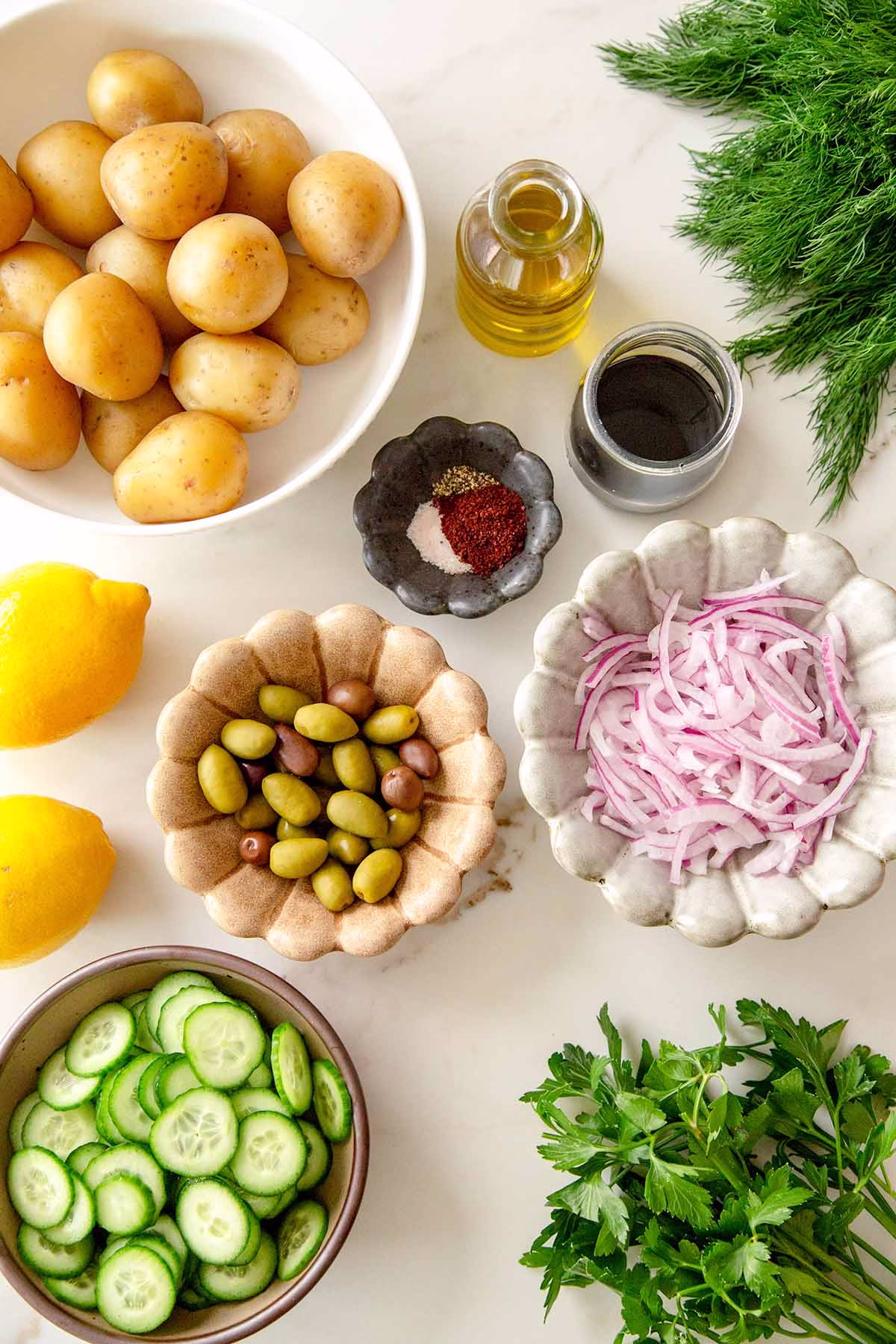 Ingredients for zesty herb potato salad laid out: baby potatoes, olive oil, lemon, sumac, fresh herbs, garlic, and salt