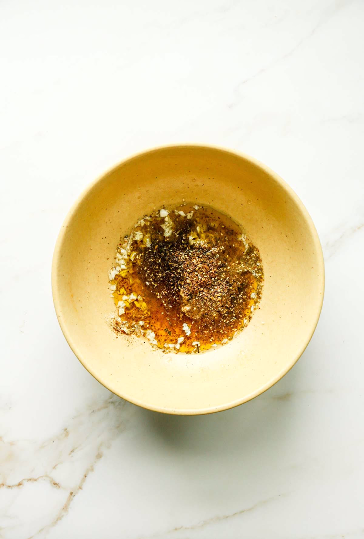 Olive oil, za’atar, lemon juice, and garlic in a yellow mixing bowl.