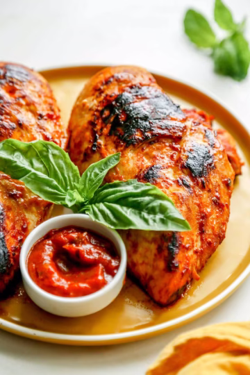 Grilled chicken with charred edges served with spicy arrabbiata sauce and fresh basil