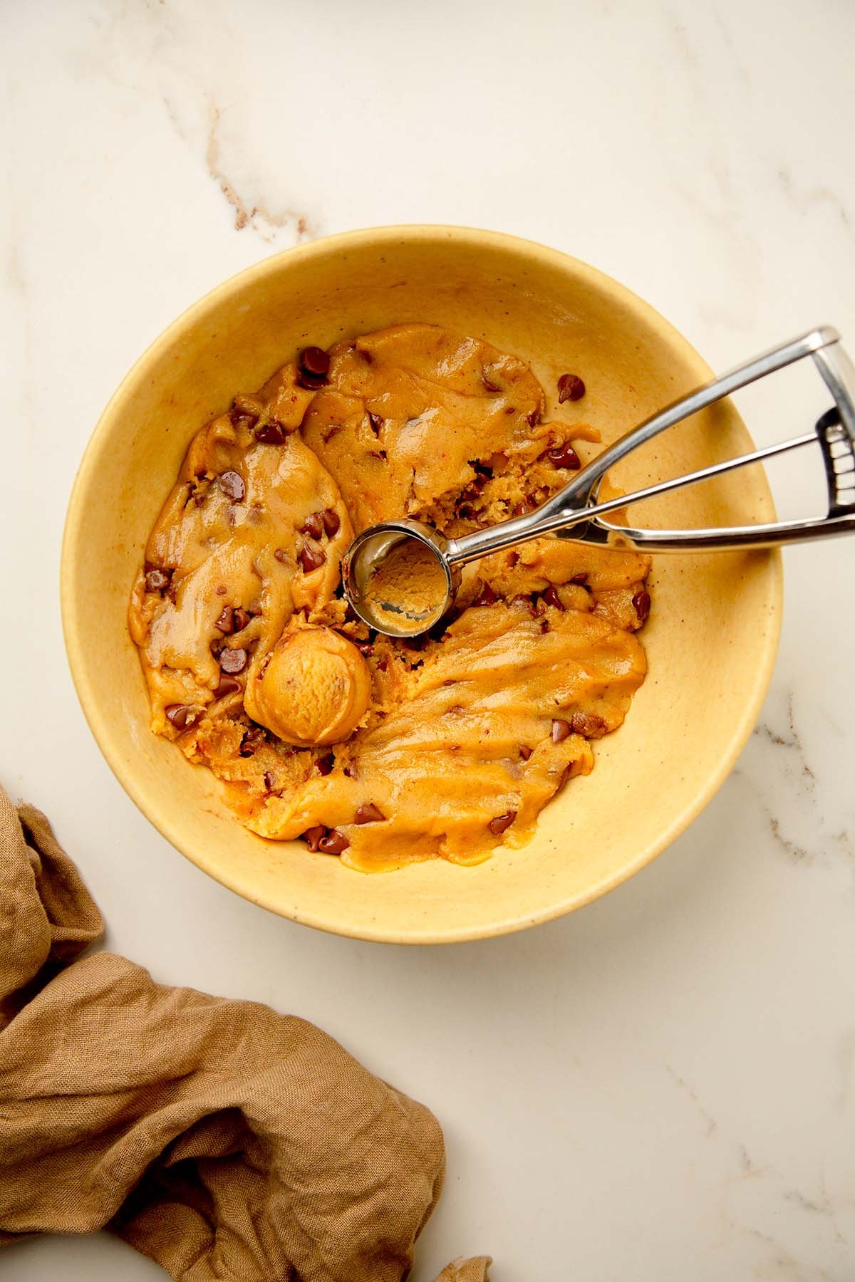 tahini chocolate chip cookie batter in a bowl with a cookie scoop