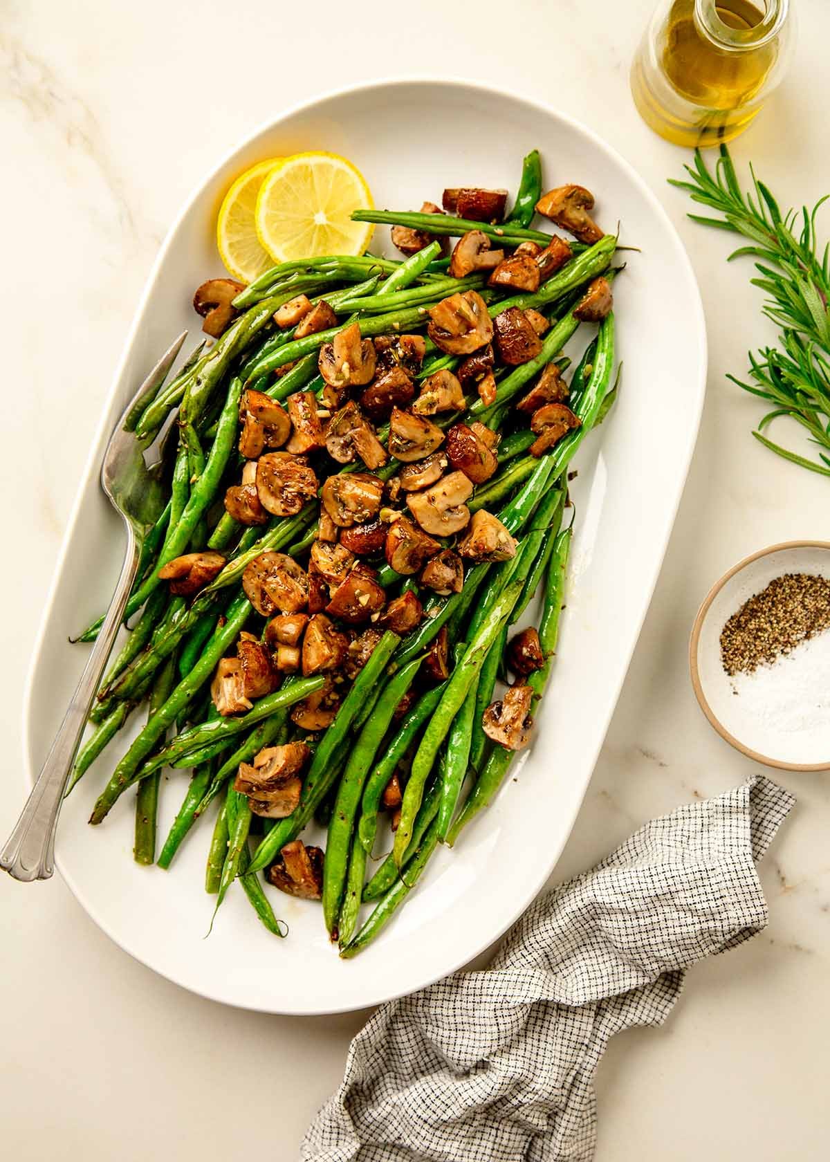 Served roasted green beans and roasted mushrooms arranges on top with slices of lemon and a large fork for serving.