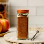 Small glass spice jar filled with Mediterranean Sweet Spice Blend with warm golden tones.