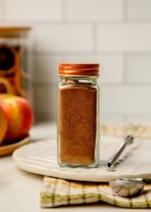 Small glass spice jar filled with Mediterranean Sweet Spice Blend with warm golden tones.