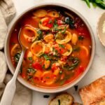 Bowl of orecchiette soup with spinach and white beans in a tomato broth.