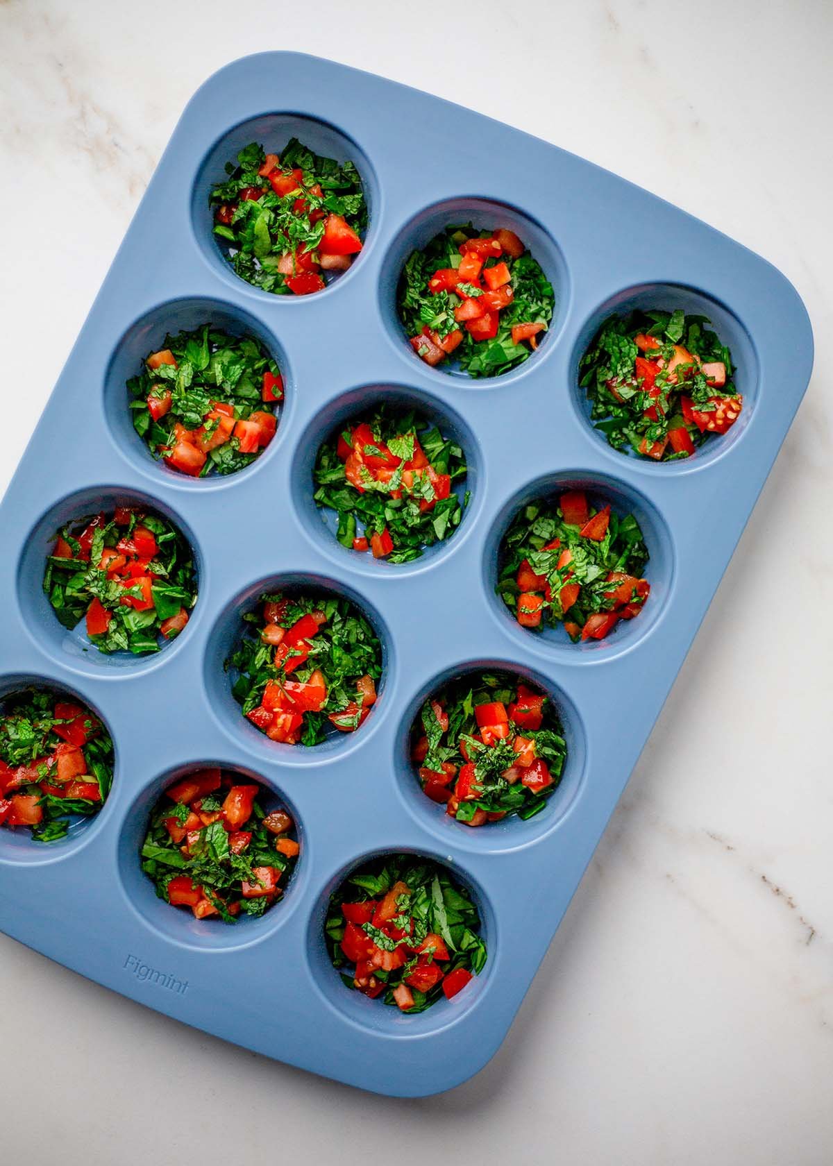 Diced tomatoes, chopped spinach, and herbs divided into muffin tin.
