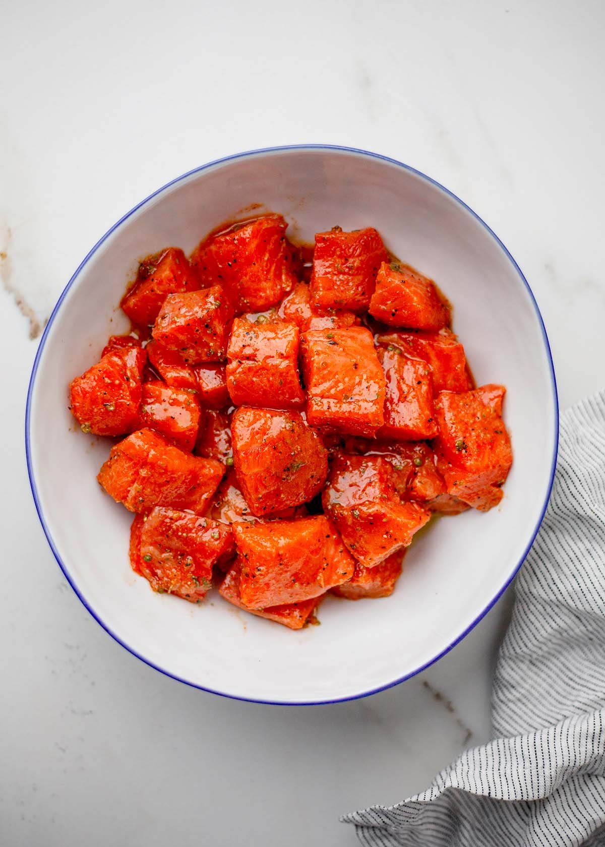 Steelhead trout bites marinating with lemon, olive oil, spices, and hot honey in a bowl.