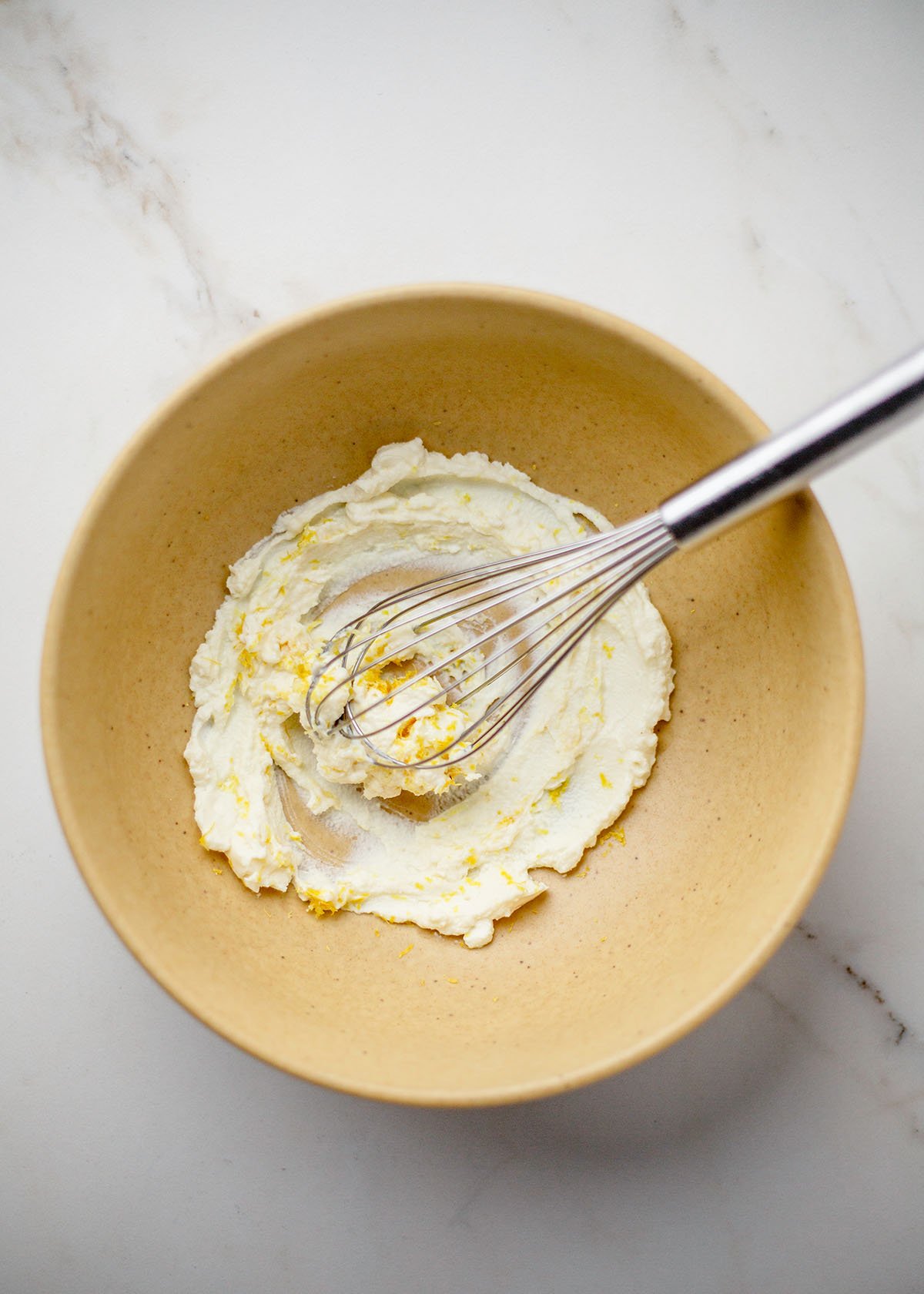 Ricotta and lemon zest whisked in yellow bowl