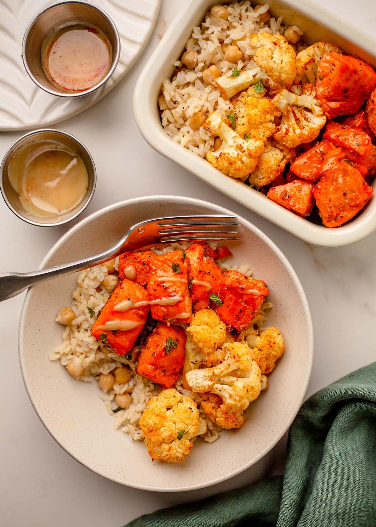 Hot honey tahini sauce drizzled over trout bites, roasted cauliflower, and brown rice in a serving bowl.