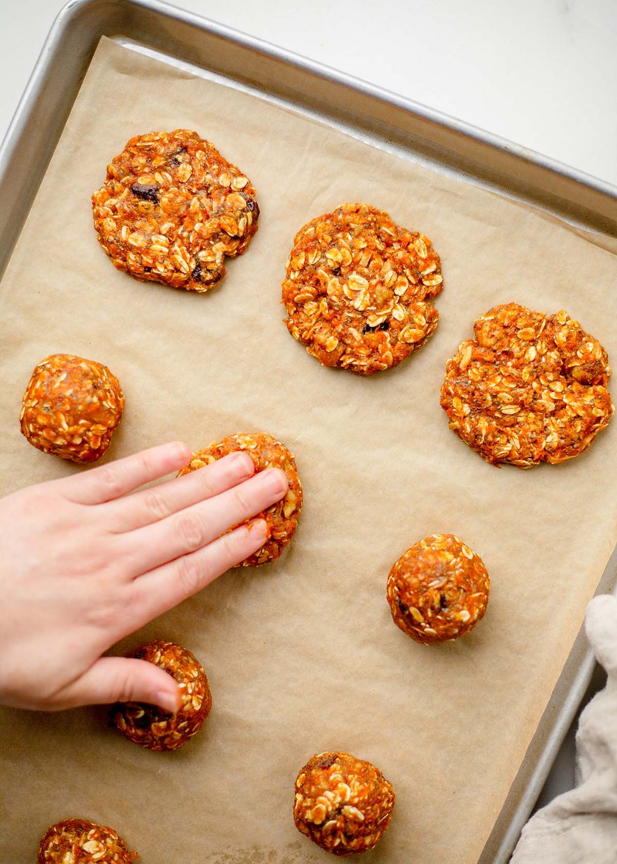Scooped morning glory cookie dough on a baking sheet using a #40 scoop. Flattening morning glory cookie dough with wet fingertips before baking.