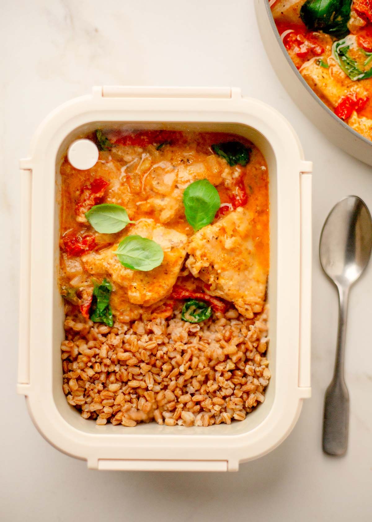 A close-up of a creamy orange sauce with chunks of chicken, sun-dried tomatoes, and fresh basil leaves in a skillet, conveying a warm, savory tone.
