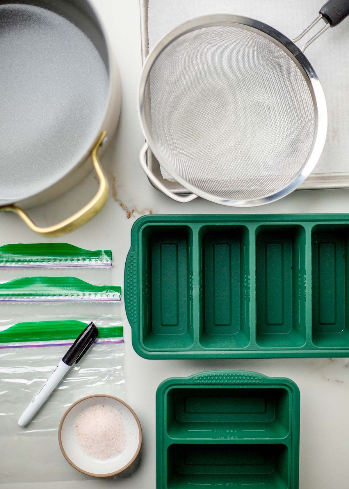 A pot, strainer, ZipLoc bags, permanent marker, sheet pan, salt, and silicone storage containers