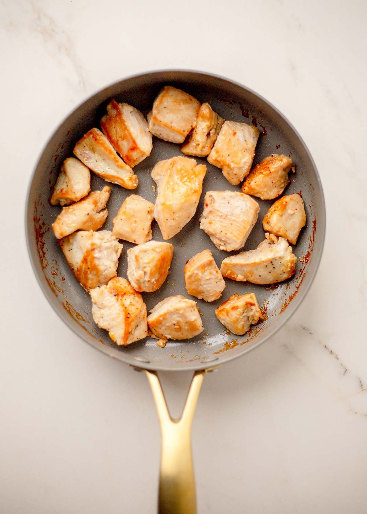 Golden-brown chicken pieces are cooked in a nonstick pan.