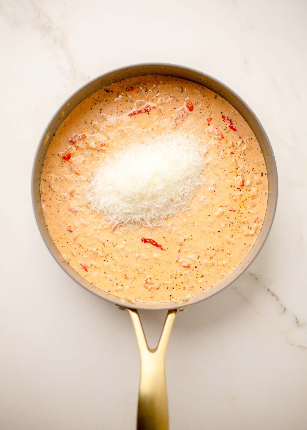 Creamy sauce in a pan, topped with a mound of grated parmesan cheese.